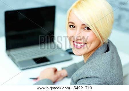 Cloeup portrait of a young smiling businesswoman looking at camera in office