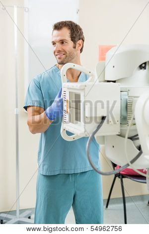 Young male nurse looking away while adjusting xray machine in examination room