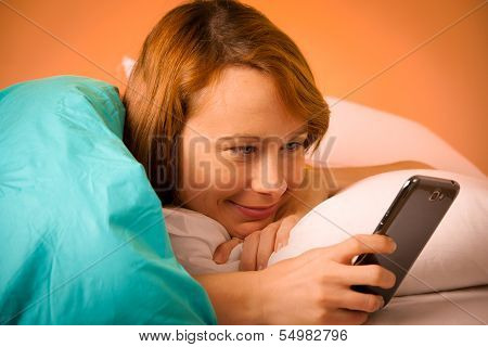Preety Woman Reading A Sms On Cell Phone In Bed