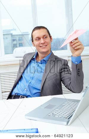 Happy businessman playing with paper plane in office