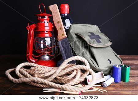 Emergency preparation equipment on wooden table, on dark background