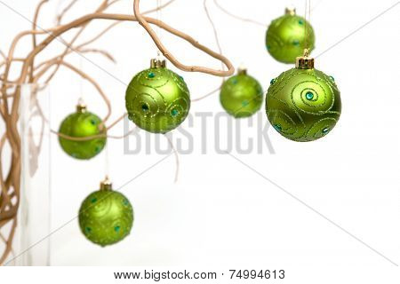 Green christmas baubles hanging from golden curly branches