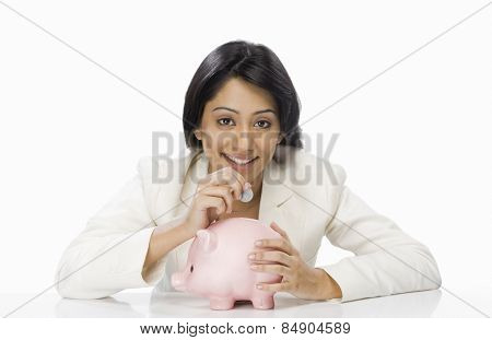 Businesswoman inserting a coin into a piggy bank