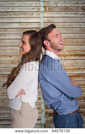 Happy young couple standing back to back against wooden background in pale wood