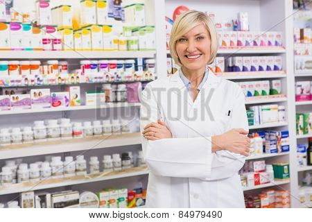 Blonde pharmacist with arms crossed smiling at camera in the pharmacy