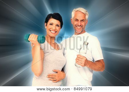 Happy fit couple with dumbbell and water bottle against abstract background