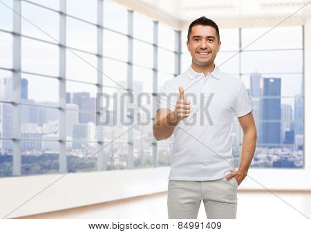 happiness, gesture, real estate and people concept - smiling man showing thumbs up over empty apartment or office room with big window and city view background