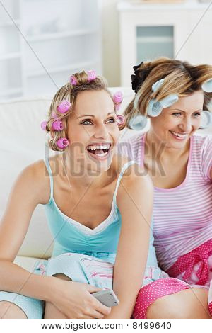 Female Friends With Hair Rollers Watching Televison On The Sofa