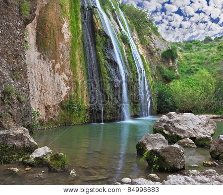 Three parallel streams of water running down the steep slope and fall in oval pool. Three-jet scenic waterfall in the mountains