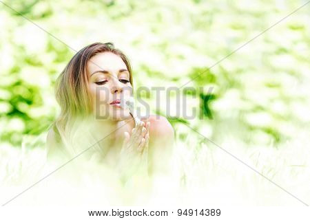 beautiful young woman iwith dandelion lying on grass
