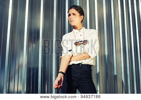 Young fashionable model standing on silver wall background while looking away