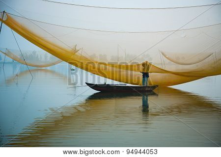 Unidentified fisher man check his nets in early morning on river in Hoian, Vietnam.