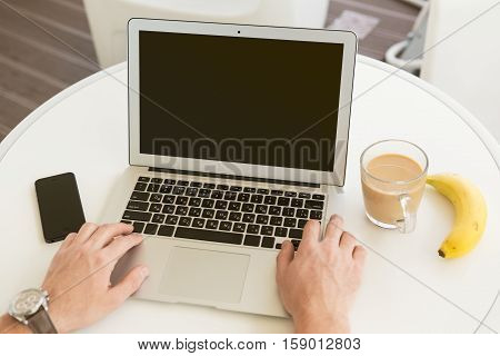 Typing on laptop in bright high-tech green office, coffee mug, bannana