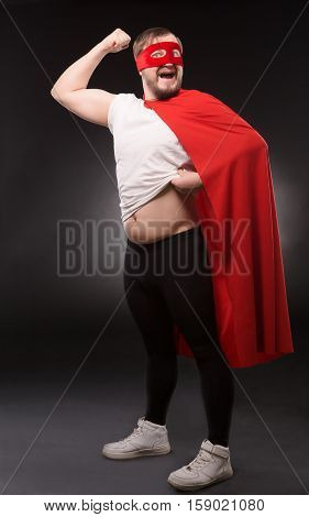 Picture of super hero man happy smiling and showing his biceps isolated on black background in studio. Handsome man showing his belly. Comic image concept of superhero.