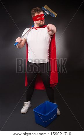 Cleaning concept. Super hero man ready to help your office or house with new cleaning equipment. Handsome man pointing to camera isolated on black background.
