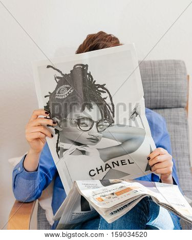 PARIS FRANCE - NOV 29 2016: Woman reading in armchari Le Monde newspaper with Chanel advertsing fashion page