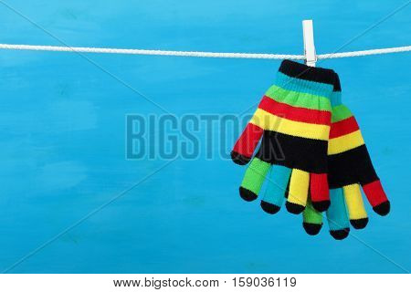 Multicolor striped gloves hanging on the clothesline on blue wooden background