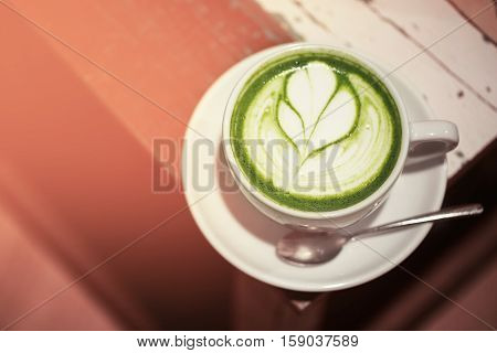 Cup of green tea matcha latte with latte art, standing on wooden rustic table.