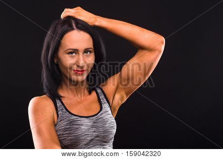 Closeup portrait of beautiful brunette fitness or sports lady smiling for camera while posing isolated on black background in studio.