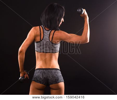 Bodybuilding concept. Fitness lady training with dumbbells while showing her muscular back isolated on black in studio. Fitness concept.