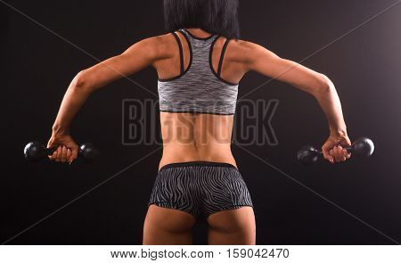 Bodybuilding concept. Picture of fitness woman training with dumbbells isolated on black. Beautiful lady showing her muscular body in studio.