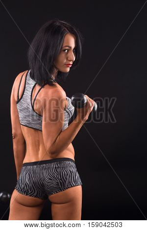 Sports concept. Pretty brunette fitness lady training with dumbbells and showing her muscular biceps and body in general in studio.