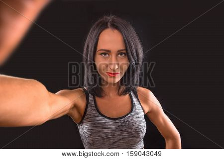 Gym concept. Muscular lady making self photos while posing for photographer. Brunette sports lady looking at camera in studio.