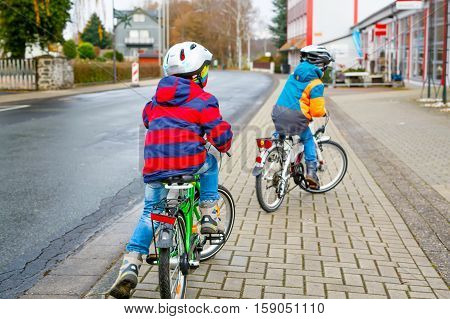 Two active kids boys in helmet biking on bicycles in the city. Happy children in colorful clothes and city traffic. Safety and protection for preschool kids. Friends making sports, acitve leisure.