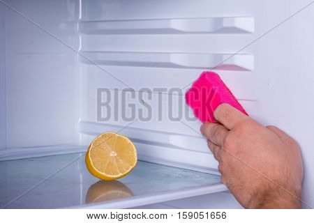 Hand and lemon cleaning refrigerator, sponge in hand