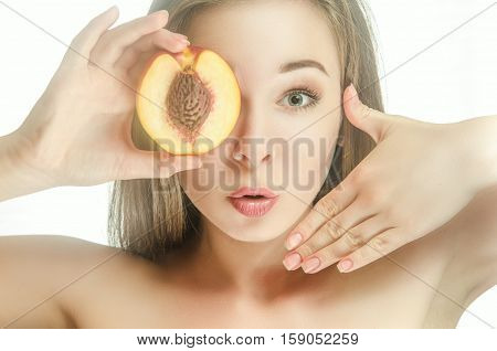 Surprised girl with half of peach. Hands raised to the face peach near the eyes like a kaleidoscope.