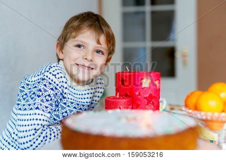 Beautiful little kid boy standing by festive table at Christmas time and holding candle. Excited child celebrating traditional . Xmas party. Catholic and christian celebration in Europe and USA