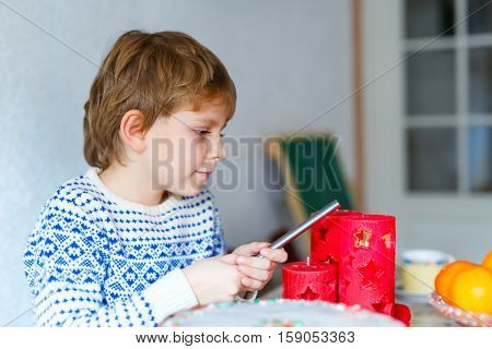Beautiful little kid boy standing by festive table at Christmas time and holding candle. Excited child celebrating traditional . Xmas party. Catholic and christian celebration in Europe and USA