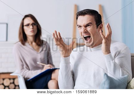 Wave of emotions. Emotional handsome oody man screamign and feeling nervous while consulting with psychologist