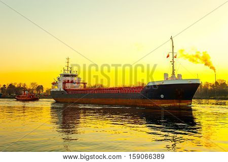 Tugboat assisting cargo ship in port at sunrsie.