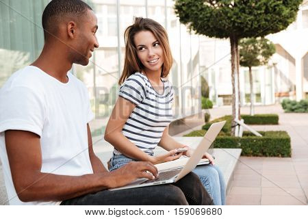 Smiling multiethnic young couple using laptop and cell phone outdoors