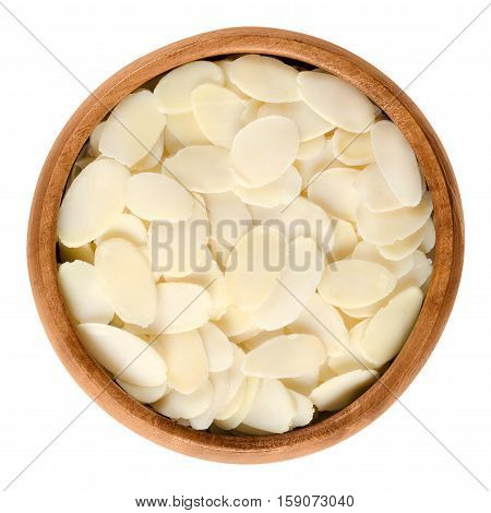 Sliced blanched almonds in wooden bowl. The light yellow raw edible seeds of Prunus dulcis are not nuts, but botanically drupes. Isolated macro food photo close up from above on white background.