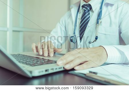 Close-up of a medical worker typing on laptop vintage tone. Doctor using laptop. Doctor using notebook. Doctor using computer. Doctor man. Doctor working. Doctor uniform.