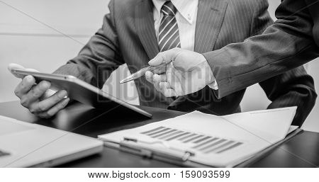 Image of two young businessmen using tablet at meeting black and white. Business working. Business room. Business man. Business woman. Business using taplet. Business using internet.