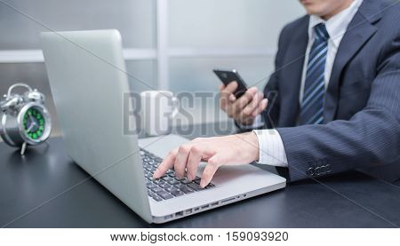 Businessman using laptop and mobile phone in office. Business using smartphone. Business using internet. Business using laptop. Business using notebook. Business using computer. Business looking smartphone.