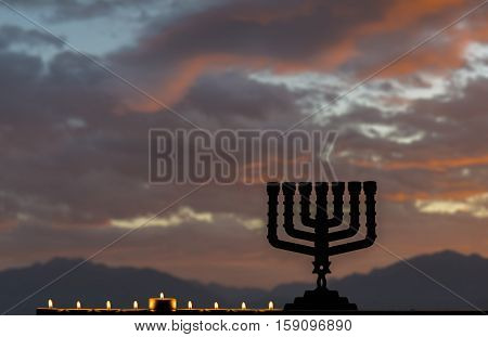 Menorah with the glitter lights of candles is traditional Jewish symbol for Hanukkah holiday. Selective focus. Mountains and cloudscape as background