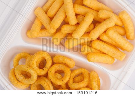 top view close up of potato and corn junk food ingredients in a white take away packaging box on yellow background calories concept