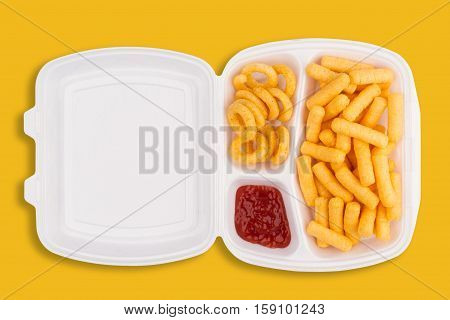 top view of junk food ingredients and a dip of ketchup in a white take away packaging box on yellow background calories concept
