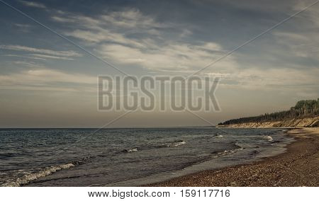 landscape with views of the Baltic Sea, on the banks of large and small stones and sand, small waves and endless horizon, blue sky and bright water, in distant cliff with pine trees, preset processed