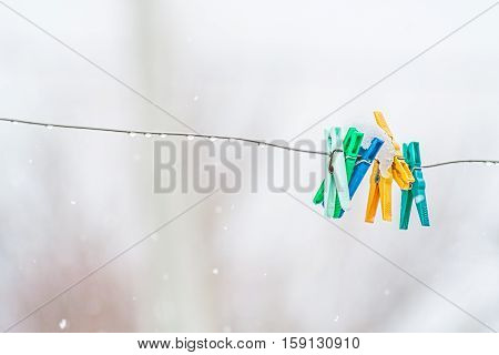 Multi-colored clothespins on an aluminum wire in the rain and wet snow close-up