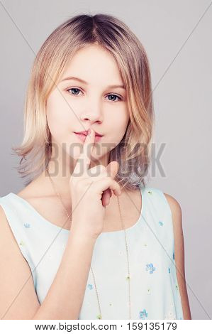 Young Girl with Blonde Bob Hairstyle. Teen Girl Holding her Finger to her Lips in a Gesture for a Secret. Female Teens Secrets