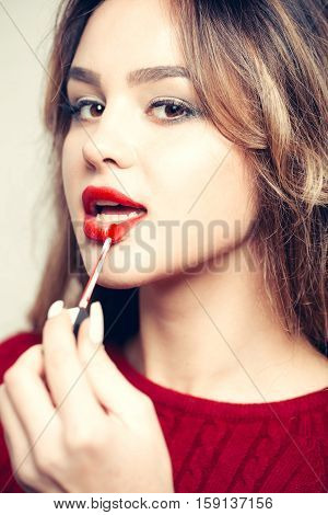 young pretty sexy woman or girl with cute face and long blond hair putting red lipstick on lips with makeup brush on white background