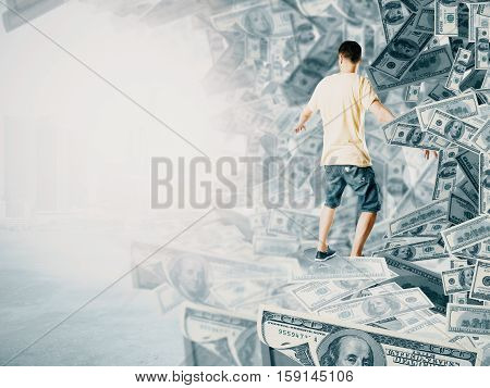 back view of young man surfing dollar banknote wave. Bright background. Success and wealth concept