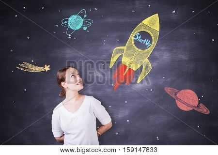 Cheerful caucasian female on chalkboard background with creative rocket ship sketch. Startup concept