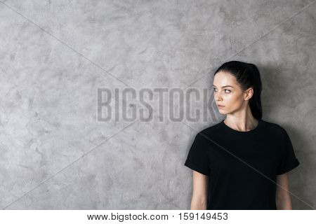 Side portrait of attractive caucasian girl in black shirt on textured concrete background with copy space
