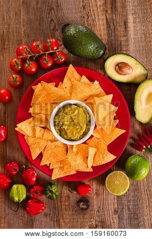 Guacamole and nacho chips on red dish.